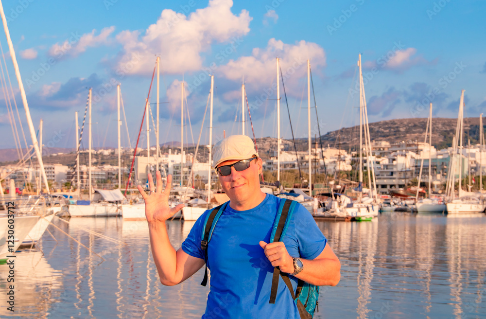 A cheerful man happily poses by the marina, surrounded by numerous sailboats under a stunning beautiful sky. Greece. Rethymnon. Crete.