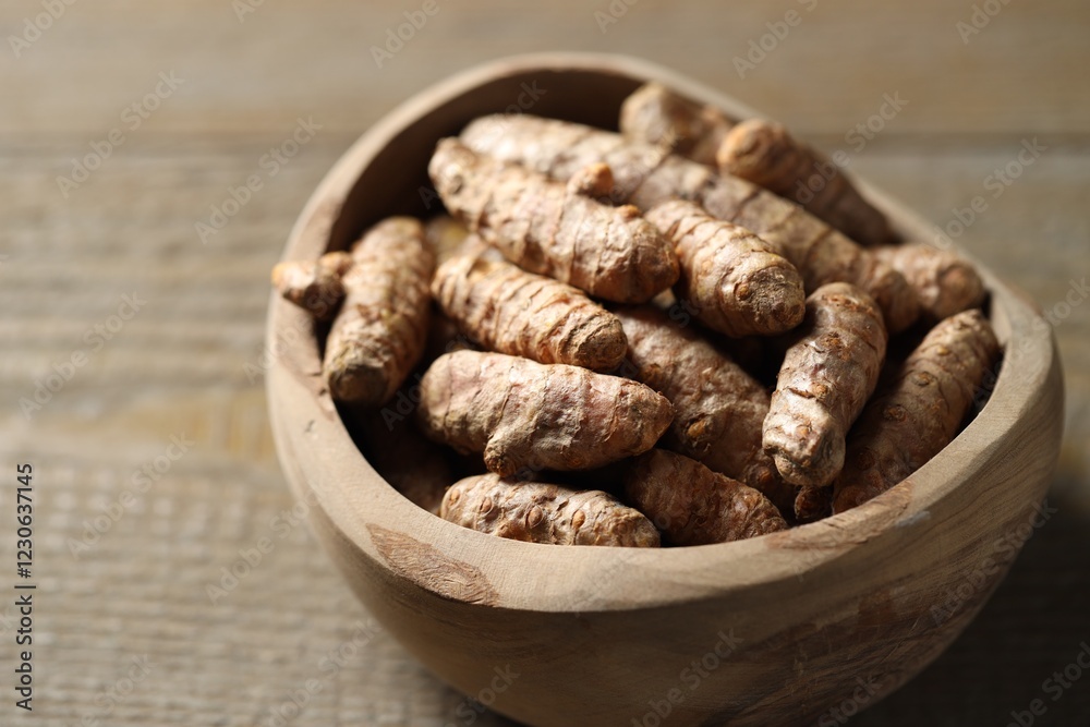 Obraz premium Raw turmeric roots in bowl on wooden table, closeup
