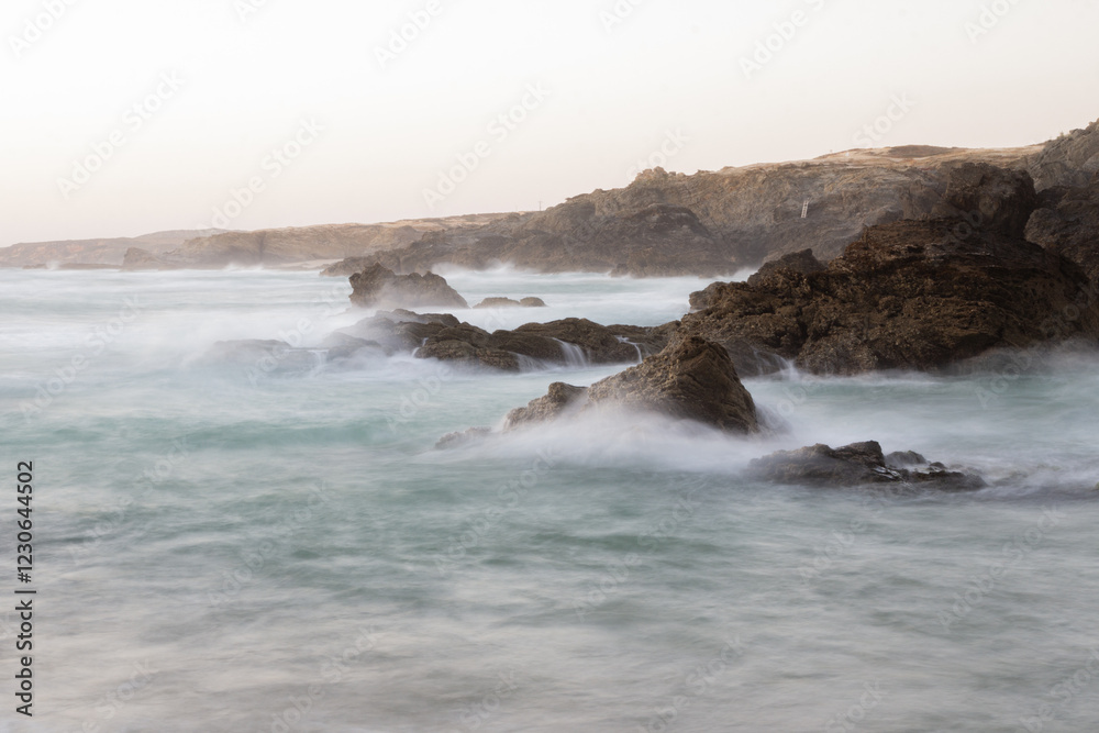 Fototapeta premium Long exposure of ocean waves crashing against rocks in Porto Covo, Portugal
