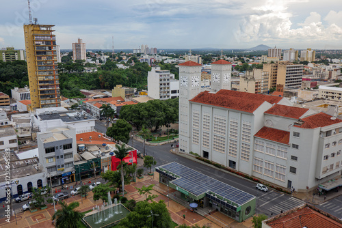Foto Vista aérea do centro histórico de Cuiabá, com a Igreja Matriz em foco, e o Morro de Santo Antônio e chuvas isoladas ao fundo