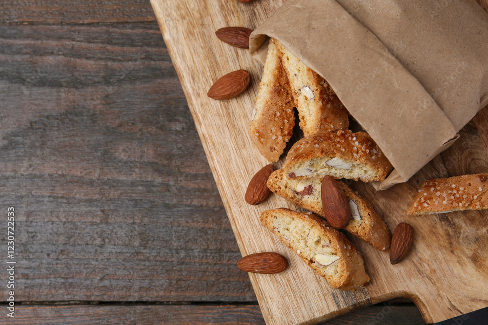Fototapeta premium Paper bag with tasty almond biscuits (Cantuccini) and nuts on wooden table, top view. Space for text