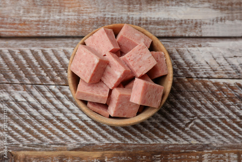 Photos Pieces of canned meat in bowl on wooden table, top view