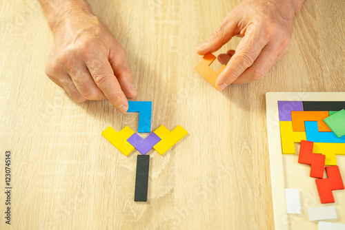 male hand manipulates colorful wooden puzzle, elderly old man composing geometric shapes, brain health and mental well-being, preventing dementia and Alzheimer's disease