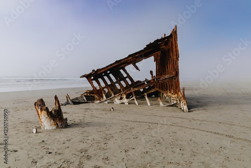 Rusty shipwreck on a foggy beach. Ocean waves crash nearby. Nature's reclamation. Wreck Of The Peter Iredale, Fort Stevens State Park, Oregon, USA