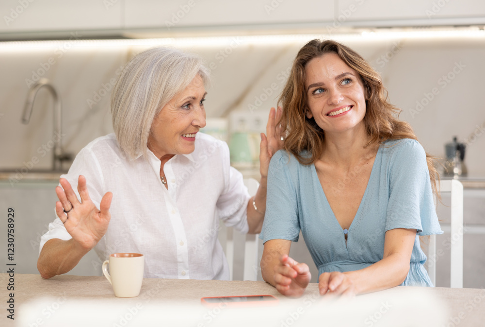Elderly mother and adult daughter drinking tea and chatting happily at home Elderly mother and adult daughter drinking tea and chatting happily at home