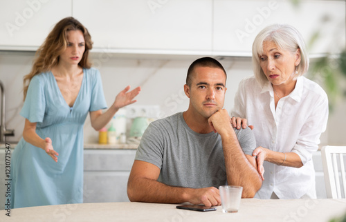 Elderly mother and young wife scold young husband while in kitchen at home photo