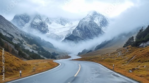 Winding mountain road leads to snowy peaks shrouded in mist and low clouds
