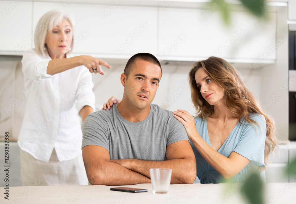 Elderly woman gets angry during quarrel with man and woman couple in kitchen Elderly woman gets angry during quarrel with man and woman couple in kitchen