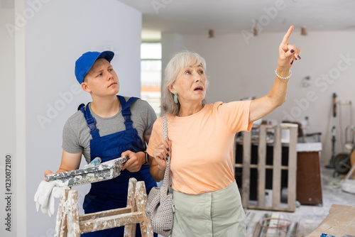 Fotografie Senior woman employer explaining work details to teenager boy who working on part-time job in construction site as painter