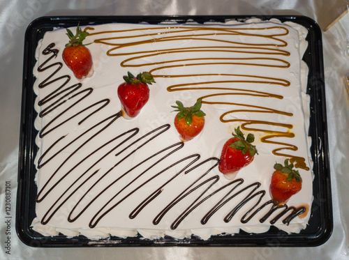 A rectangular strawberry cake covered with whipped cream, strawberries and caramel coulis