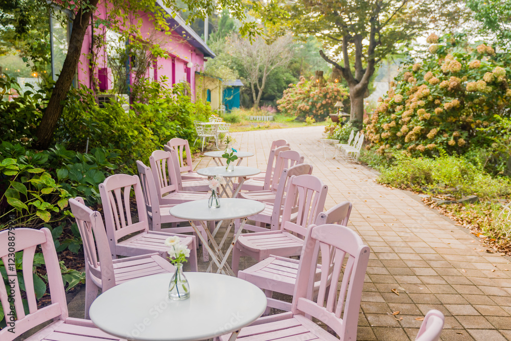 Fototapeta premium Pink chairs and round tables arranged on a floral patio, offering serene seating.
