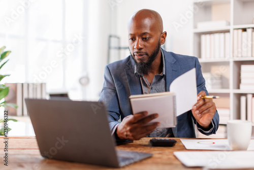 An office scene showing a professional at his desk, using a laptop for various business activities and strategies.African American Businessman work.