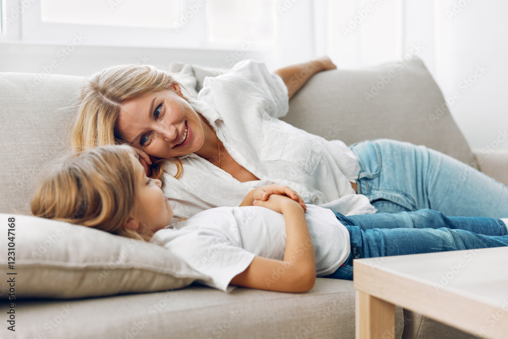 Mother and daughter bonding moment on cozy couch while watching television in a comfortable living room setting Mother and daughter bonding moment on cozy couch while watching television in a comfortable living room setting