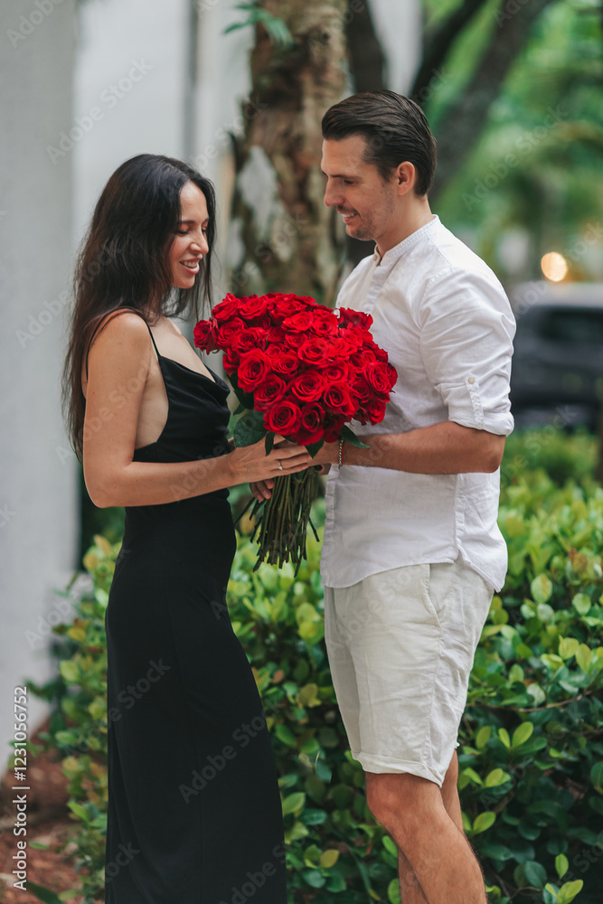 Young man gives his girlfriend a bouquet of red roses on Valentine's Day. The girl is wearing an elegant black dress. Valentine's Day Flowers