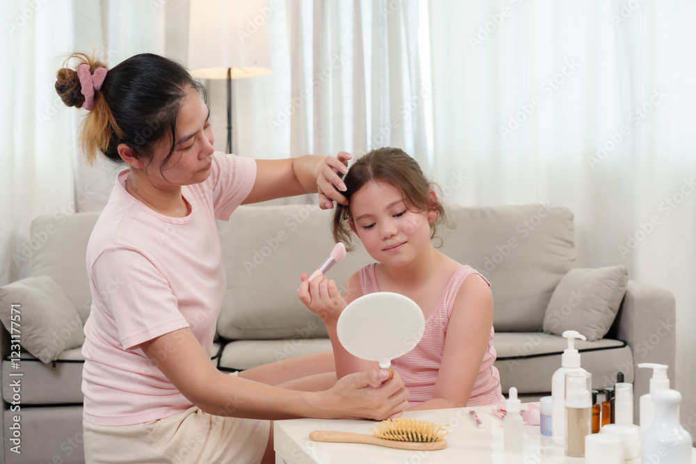 Happiness of Caucasian daughter and Asian mother as they practice beauty routines. Daughter holding a makeup brush while mother adjusts her hair, creating a loving and fun moment at home. Happiness of Caucasian daughter and Asian mother as they practice beauty routines. Daughter holding a makeup brush while mother adjusts her hair, creating a loving and fun moment at home.