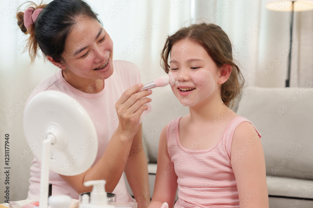 Happiness of Caucasian daughter and Asian mother as they laugh while applying blush. Mother playfully dabs daughter’s cheek with a makeup brush, enjoying a fun and affectionate moment together. Happiness of Caucasian daughter and Asian mother as they laugh while applying blush. Mother playfully dabs daughter’s cheek with a makeup brush, enjoying a fun and affectionate moment together.