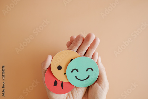 Hands holding sad face hiding behind happy face, bipolar and depression, mental health, split personality, mood change concept