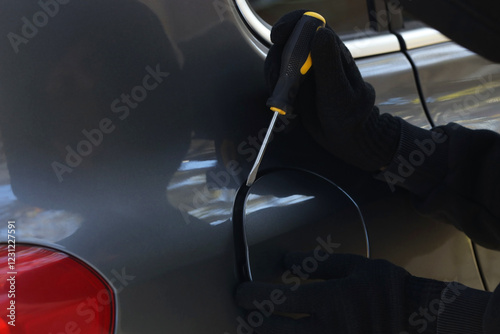 Thief with screwdriver opening fuel cap, closeup. Car hijacking