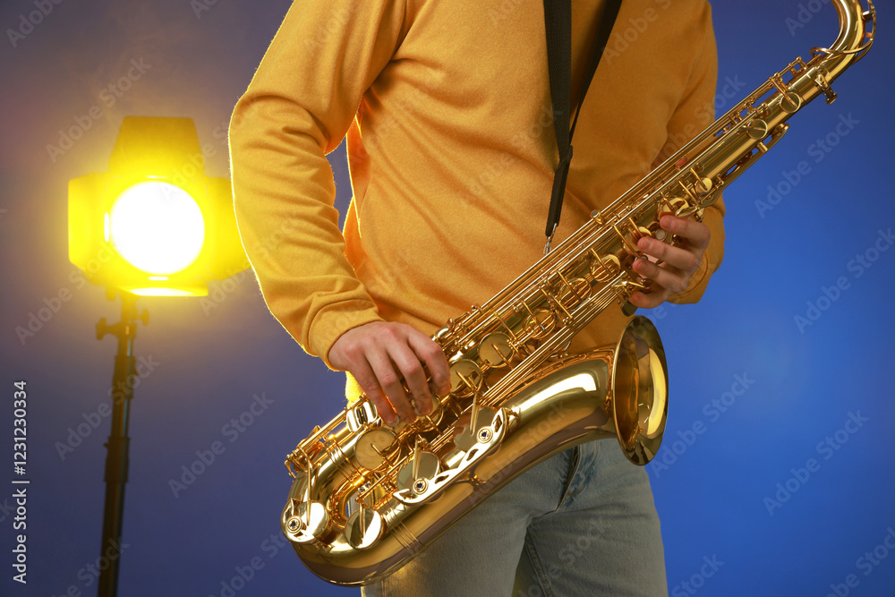 Obraz premium Professional musician playing saxophone on blue background with light, closeup