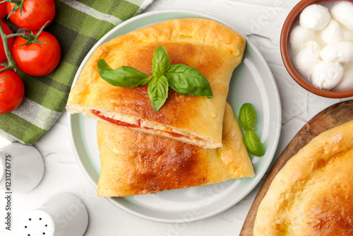 Pieces of tasty vegetarian calzone with tomatoes, mozzarella cheese and basil on white textured table, top view