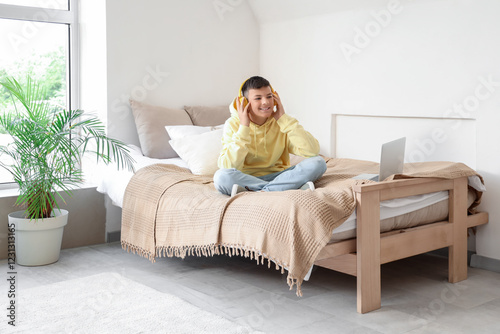 Teenage boy in headphones sitting on bed at home