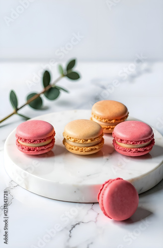 on a marble round tray there are orange and pink macroons, next to a eucalyptus branch photo