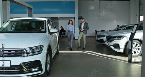Wallpaper Mural A car dealership manager in formal clothes talks to a customer and shows him a car standing in the showroom Torontodigital.ca