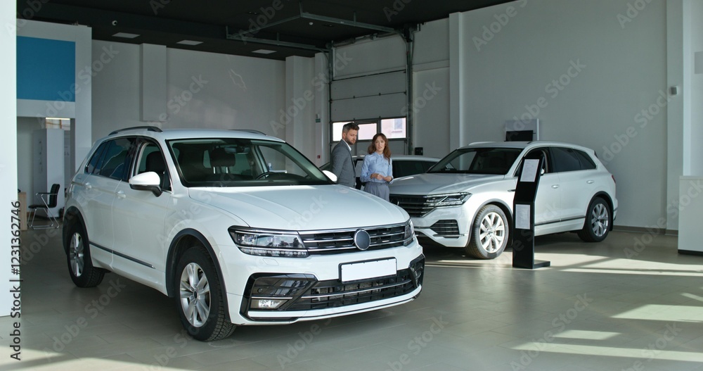 The car dealership manager talks to the customer standing near the car in the showroom The car dealership manager talks to the customer standing near the car in the showroom