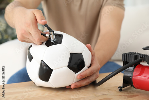 Man inflating soccer ball with air compressor indoors, closeup photo