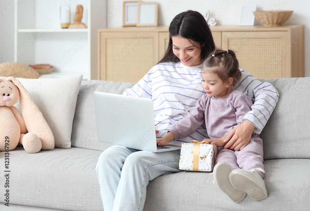 Young mother and her little daughter with gift box using laptop on sofa at home Young mother and her little daughter with gift box using laptop on sofa at home