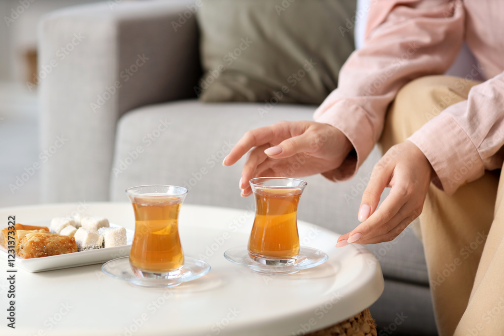 Young woman taking glass of Turkish tea from table at home, closeup Young woman taking glass of Turkish tea from table at home, closeup