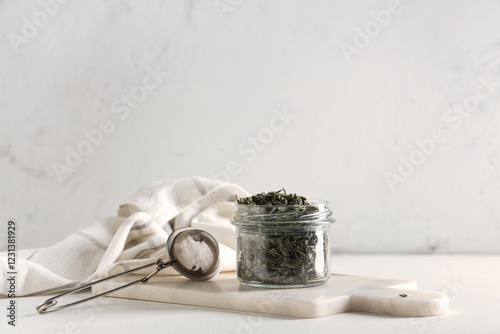 Photography Jar with dried green tea leaves and strainer on white background
