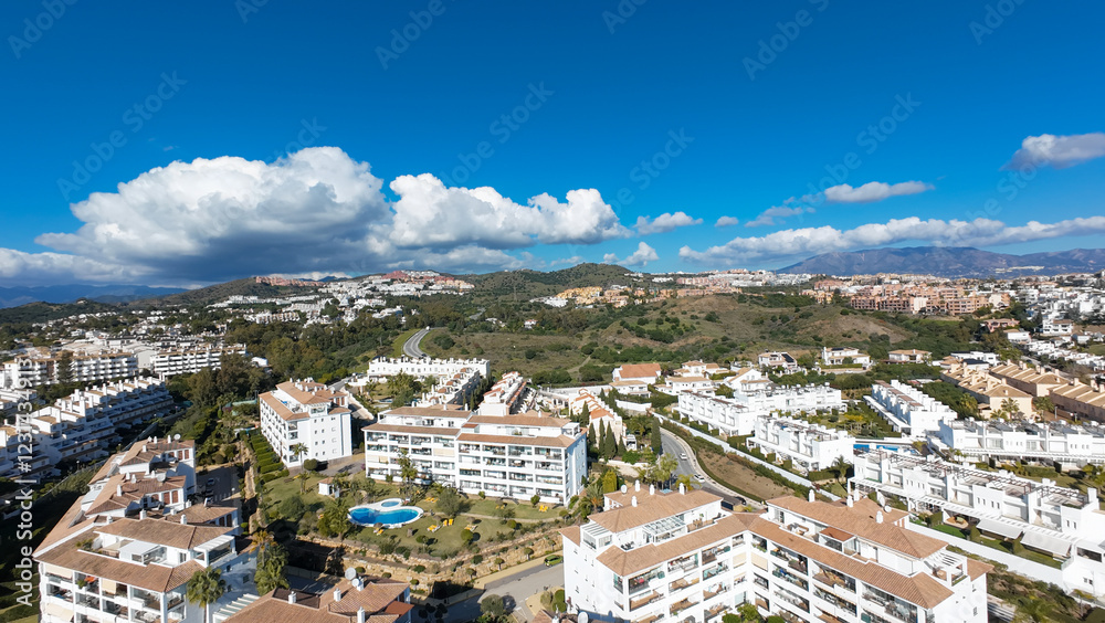 Naklejka premium Aerial drone photo of the beautiful town of Sitio de Calahonda taken in the winter time showing residential and holiday homes with swimming pools from above and the mountains in the background