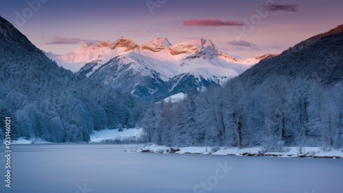 Alpine lake reflecting snow-capped mountains at dawn with soft pink and purple hues in the sky surrounded by frosted trees in a winter landscape