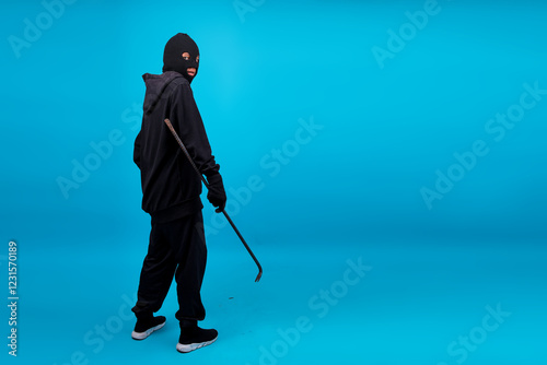 Εκτύπωση καμβά Full Length Thief In Hood Wearing Balaclava Holding Crowbar Isolated On Blue Bac