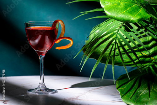 Bijou alcoholic cocktail drink with gin, sweet vermouth, liqueur and orange bitters. Marble table, blue background with tropical leaves