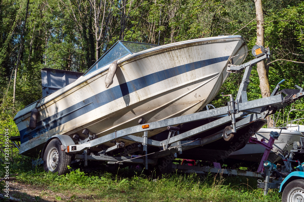 Boat is sitting on a trailer in a grassy area. The boat is dirty and has a trailer attached to it Boat is sitting on a trailer in a grassy area. The boat is dirty and has a trailer attached to it
