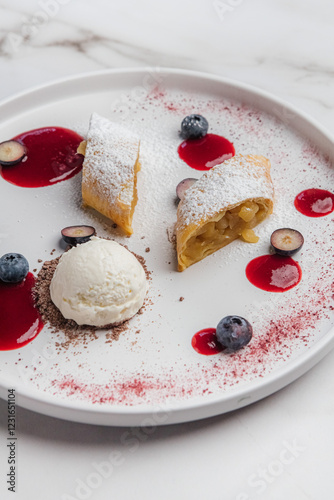 Apple strudel with powdered sugar, accompany a scoop of vanilla ice cream, drizzled with berry coulis and topped with fresh blueberries and chocolate shavings. Restaurant or cafe menu, cookbook recipe