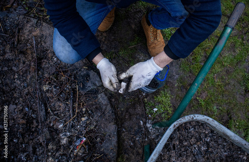 A man carefully uses a magnet to collect steel, screws, and other metal parts, gathering them into a plastic bottle for recycling. This hands-on effort helps organize the yard and keep it clean.