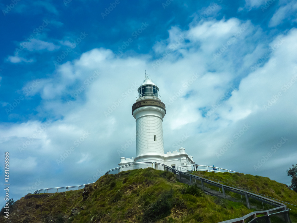 Close-up view of iconic Cape Byron Lighthouse rising against cloudy dramatic sky in New South Wales, Australia. Distinctive white tower and lantern room. Tourist attraction along coastal hiking trail Close-up view of iconic Cape Byron Lighthouse rising against cloudy dramatic sky in New South Wales, Australia. Distinctive white tower and lantern room. Tourist attraction along coastal hiking trail
