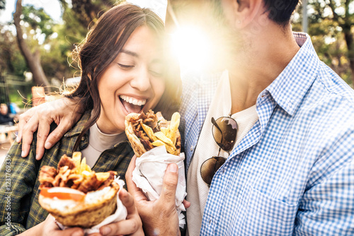 Happy couple eating gyros souvlaki  wrapped in a pita, greek food - Smiling girl and guy bite Doner kebab outside