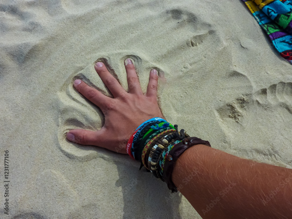 Hand with colorful friendship bracelets and wristbands making an imprint in pristine white sand on Great Keppel Island beach, Queensland, Australia. Perfect palm impression against bright sunlit beach