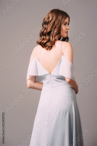 Gorgeous young lady in blue bardot evening dress, rear view. Sensual studio portrait of brunette woman. Bardot backless gown, elegant look. Romantic bridesmaid's summer outfit