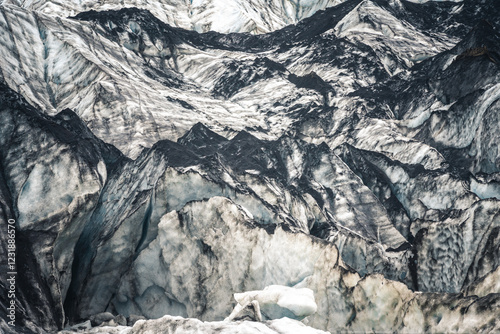 Gros plan sur un glacier islandais, dévoilant ses strates de glace bleutée marquées par les cendres volcaniques. Reliefs sculptés par le temps et reflet dans le lac glaciaire créent un contraste saisi photo