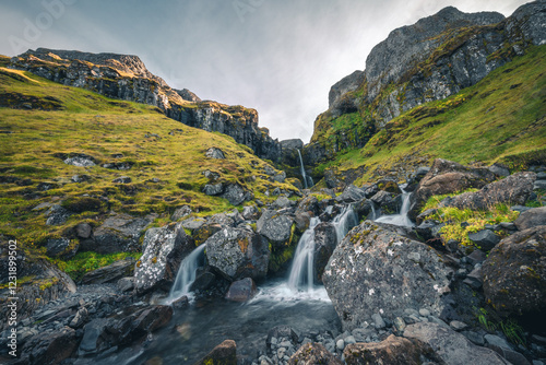 Fotografija Cette magnifique cascade islandaise s’écoule en plusieurs niveaux le long d’une falaise verdoyante, entourée de roches volcaniques et d’une nature sauvage intacte