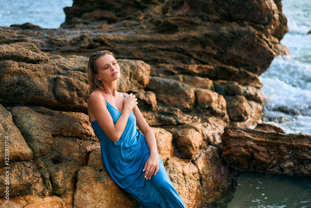 Stunning model woman in wet dress poses on rocky shore of exotic island. Ocean waves crash nearby. Luxury fashion, beauty, cosmetics, fragrance trend. Elegant, serene, tropical vibes. Stunning model woman in wet dress poses on rocky shore of exotic island. Ocean waves crash nearby. Luxury fashion, beauty, cosmetics, fragrance trend. Elegant, serene, tropical vibes.