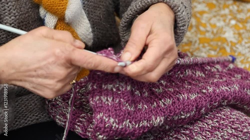 Person is knitting a purple sweater with a striped pattern. The person is using a knitting needle to work on the sweater