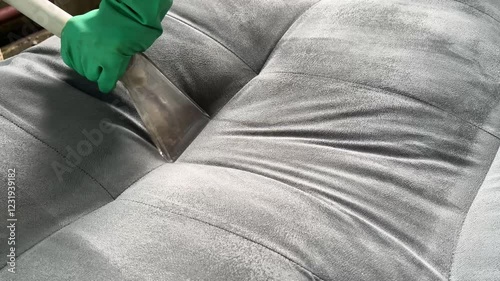 The process of cleaning sofa using extractor to refresh and clean from dust and stains upholstered furniture. Cleaner is dry-cleaning sofa using extractor machine with detergent