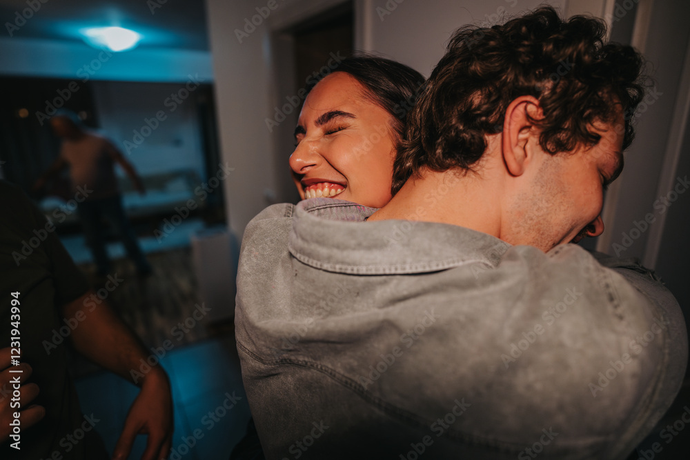 A smiling woman enjoys a warm hug from a friend at a casual indoor gathering, radiating happiness and friendship in a cozy setting. A smiling woman enjoys a warm hug from a friend at a casual indoor gathering, radiating happiness and friendship in a cozy setting.