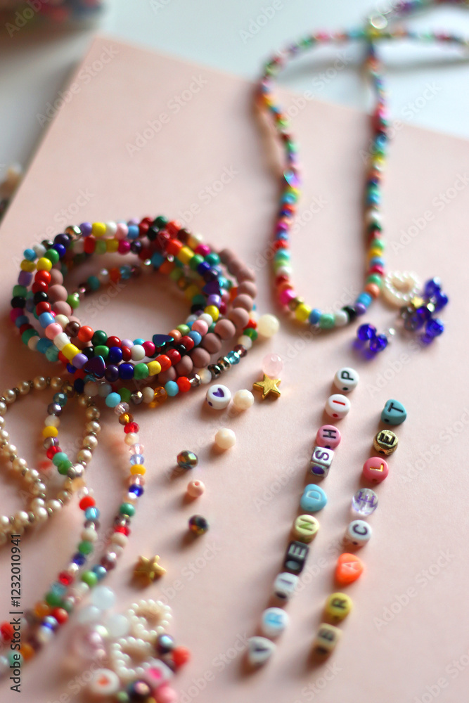 Friendship bracelet spelled with letter beads. Colorful handmade bracelets and various beads. Selective focus, pink background.